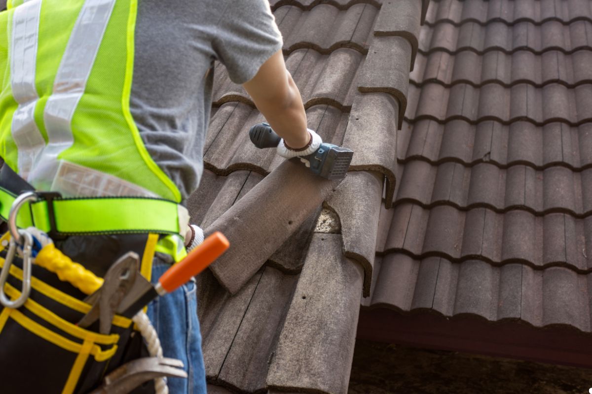 A man using a tool while working on a roof, focused on his task under a clear blue sky.