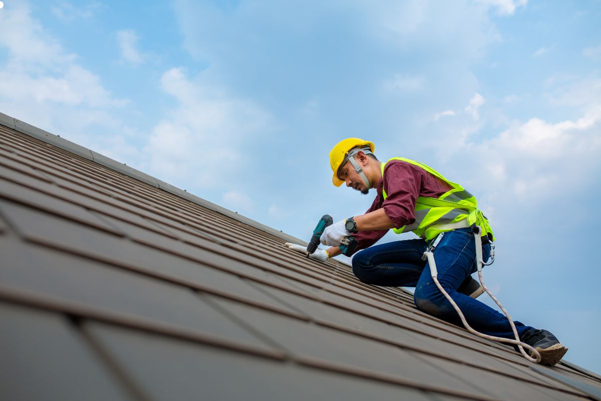 A man in a yellow safety vest inspects various roofing materials on a residential roof.